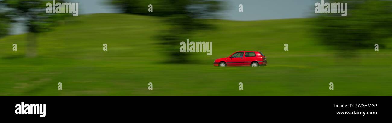 A red Volkswagen Golf drives through a green landscape, Bayersoien, Bavaria, Germany Stock Photo