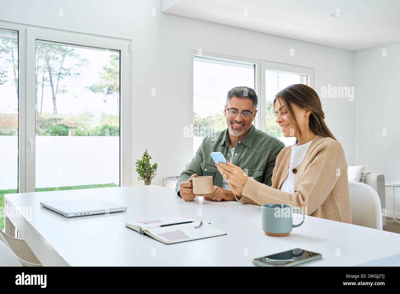 Middle aged happy couple using smartphone relaxing at living room table at home. Stock Photo