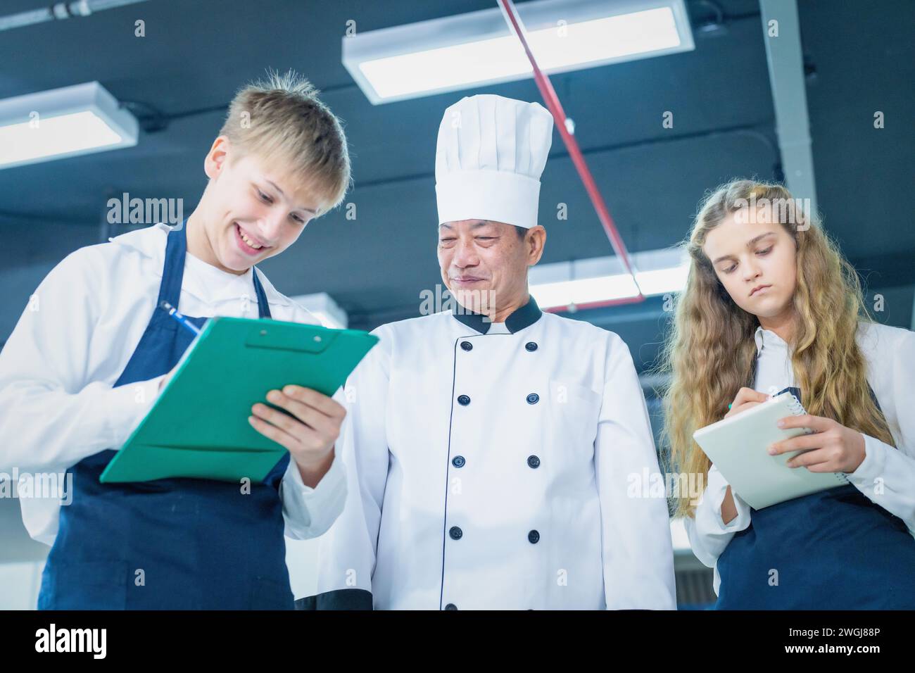 Senior male chef teaches young teenage boys cooking in school kitchen. Education Concept Stock Photo