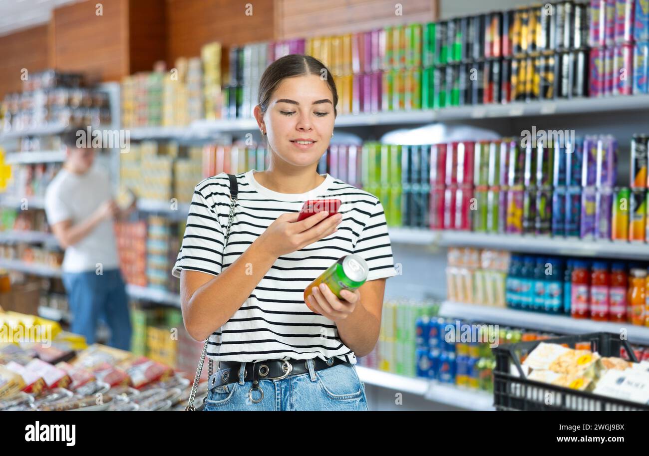 Girl scanning QR code on can of soft drink with smartphone in grocery