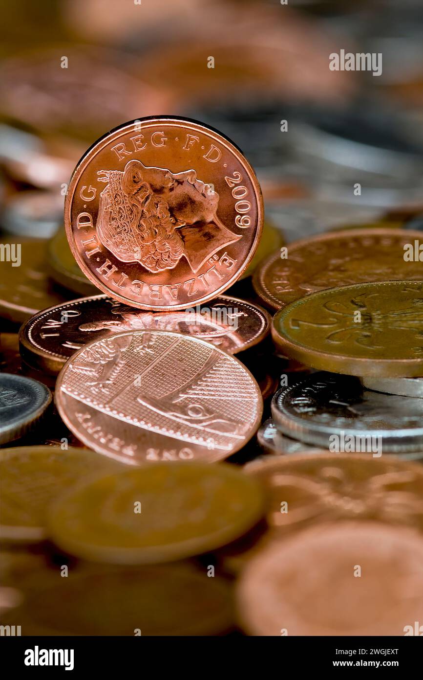Studio shot of a one penny piece in Sterling currency standing upright on a table full of loose change with out of focus coins in foreground Stock Photo