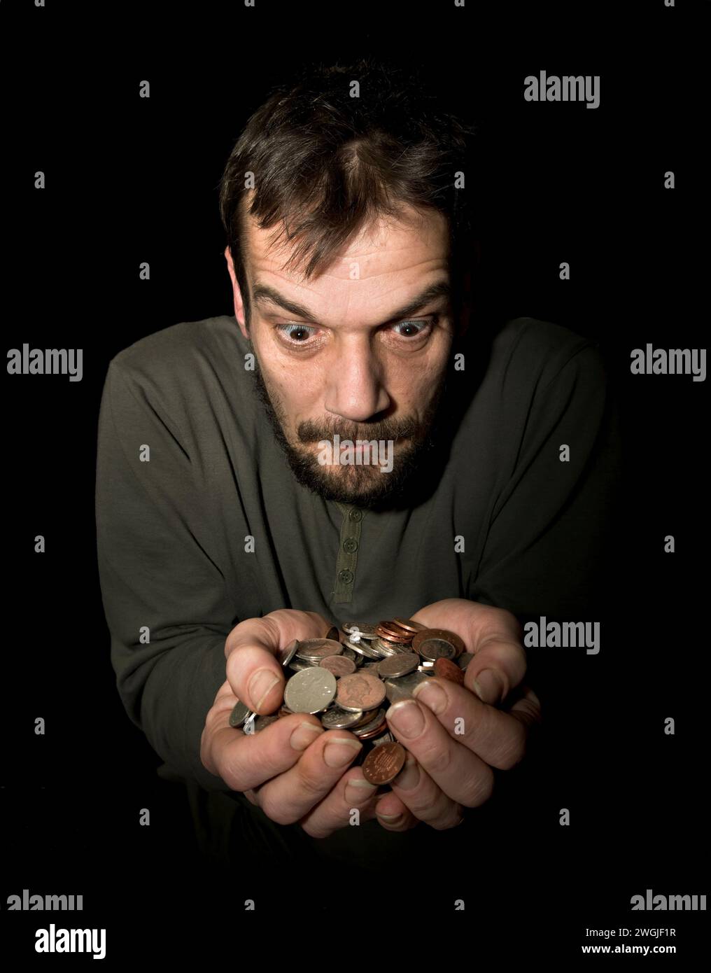 Caucasian Male (42 years old) with hands held out crammed full with loose change in sterling currency with greedy look on face Stock Photo