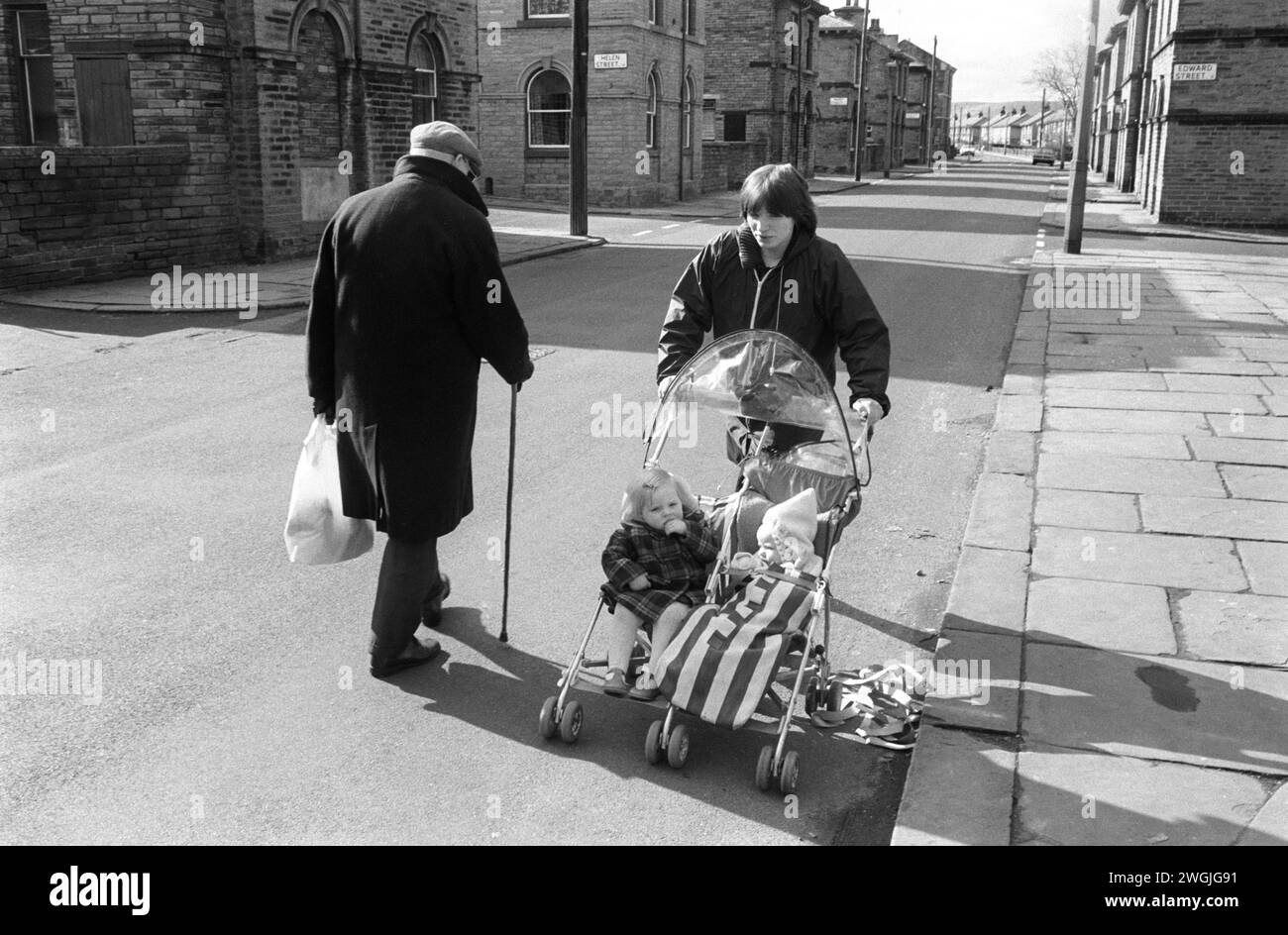 Mother pushing pram in road 1989s UK. Cobbled pavement makes the pram shake, old man walking in road for safety, he’s afraid of falling on uneven pavement. No cars no yellow lines.  Shipley, Bradford West Yorkshire England 1981. Saltaire was a Victorian Model village built around the Salts Mill named after Sir Titus Salt.  It was closed down in 1986  after 133 years as a textile factory. Now a UNESCO World Heritage Site HOMER SYKES Stock Photo