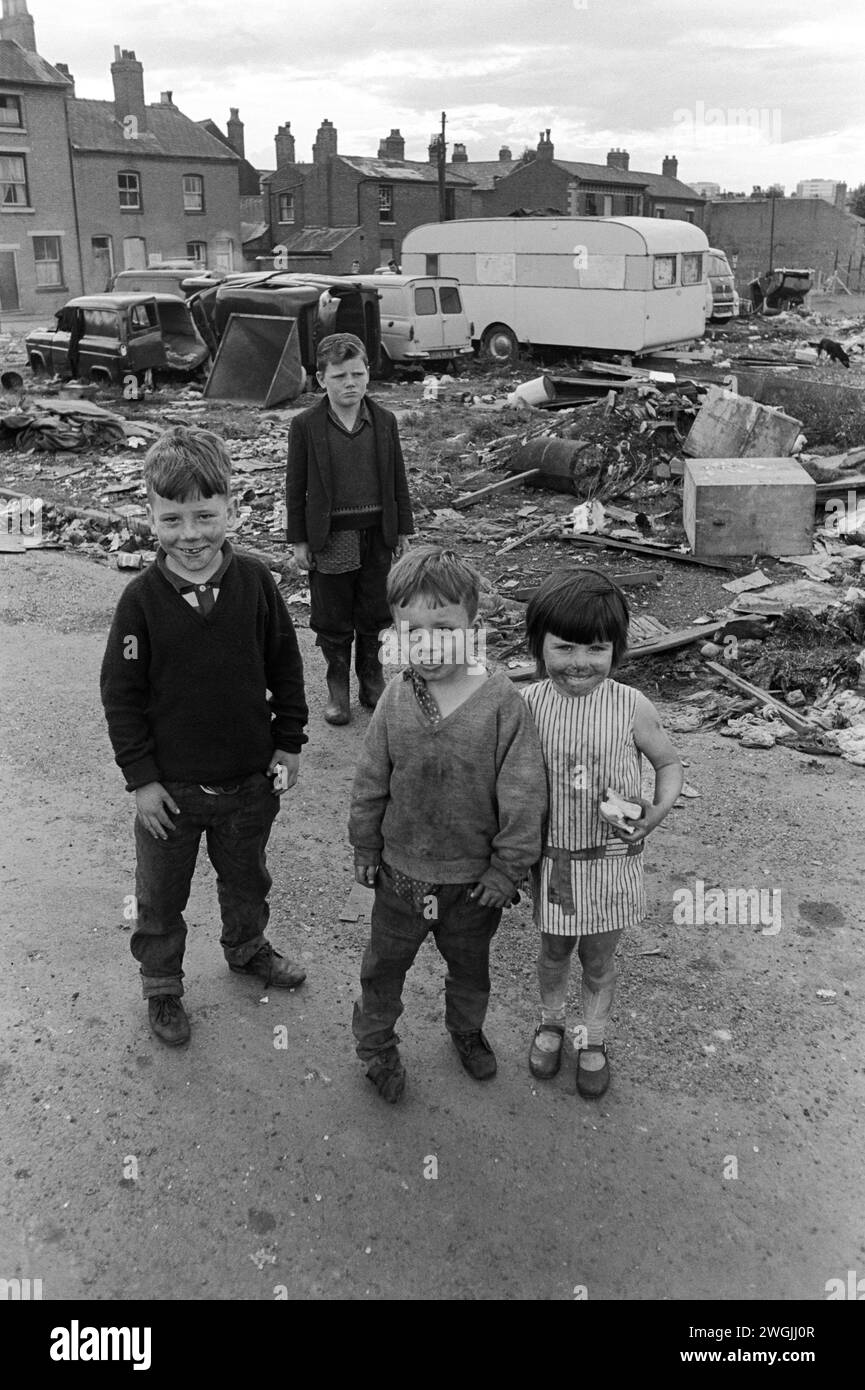 Irish Travellers children 1960s UK. Gypsy Irish traveller kids, their encampment on city centre wasteland Balsall Heath. Their caravan in background.  Parents and other tinkers are making money out of scrap metal – scrap cars. The houses are on Emily Street. Birmingham, England March 1968.  1960s UK  HOMER SYKES Stock Photo