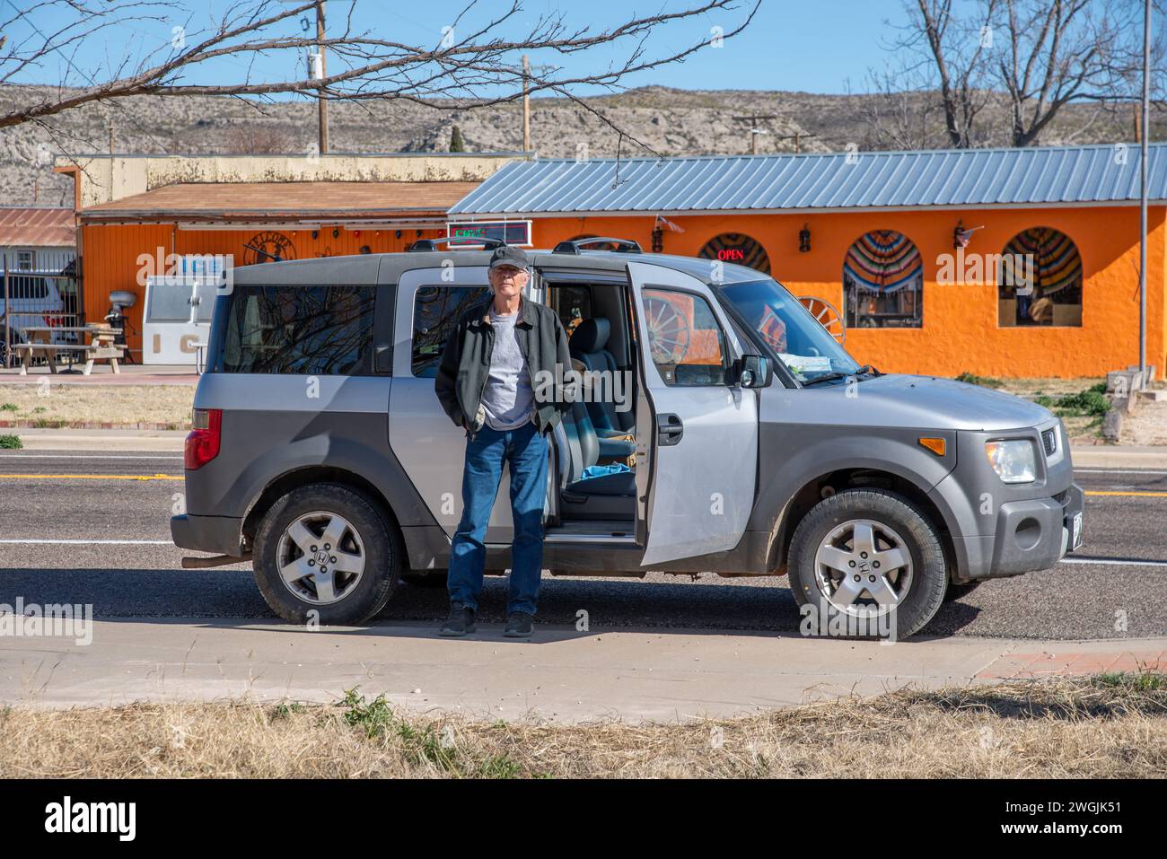 Senior male casually stands by his car, a grey 2004 Honda Element, with his hands in his pockets, Sanderson, Texas, USA. Stock Photo