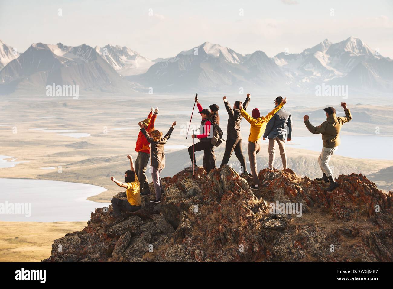 A large group of diverse tourists celebrates the completion of their climb to the top of the mountain with great view at sunset. Mixed ages and skills Stock Photo