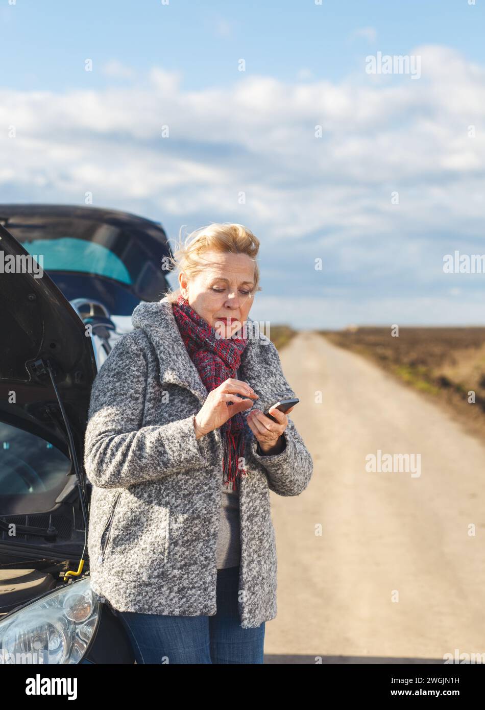 Senior woman on the road having engine failure, she is calling for assistance. Stock Photo
