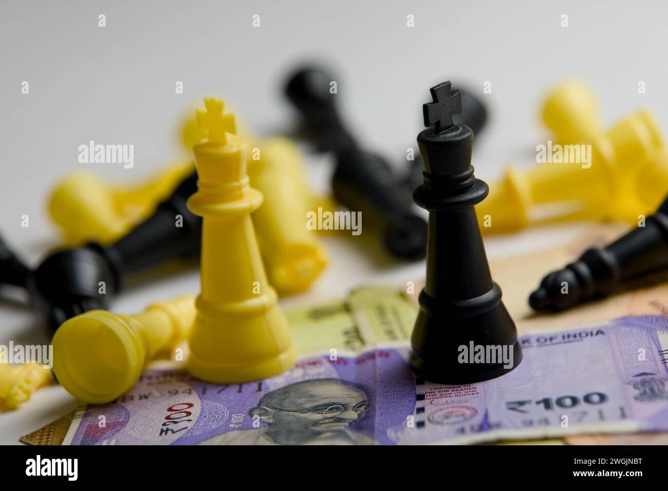 A strategic still life showcasing chess pieces locked in battle on a stark white backdrop, intermingled with stacks of coins and bills Stock Photo