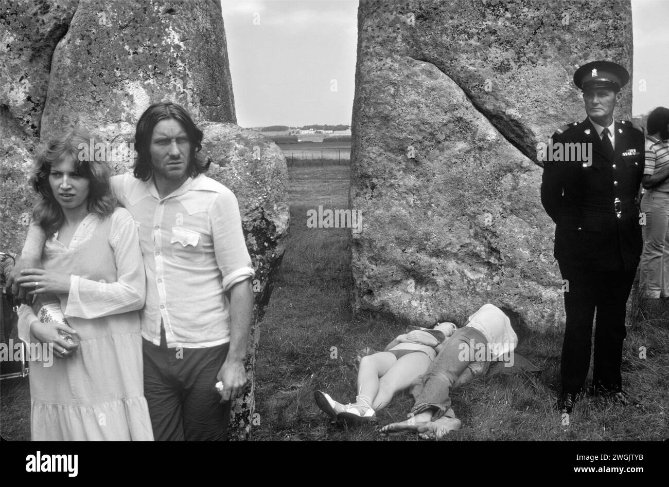 Stonehenge Free Festival at the summer solstice, Wiltshire, England June 21st 1979. Besides the hippies a small group of English tourists watched as others lay in the sun and a 'guard' stood by watching. 1970s UK HOMER SYKES Stock Photo