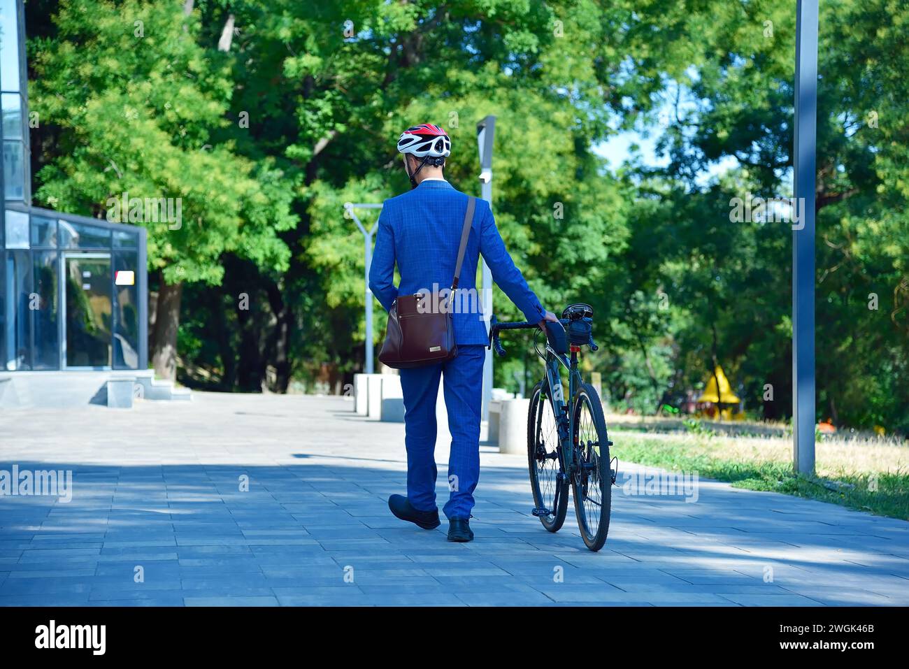 Young businessman in blue suit and helmet with bike walking in park. Business and urban style concept. Stock Photo