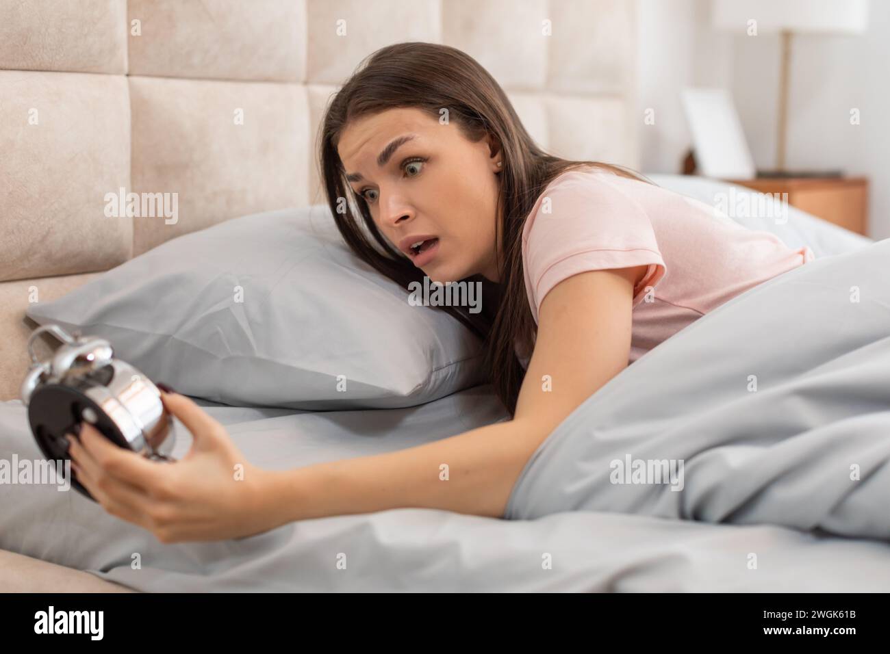 Shocked woman looking at an alarm clock in bed in the morning Stock Photo