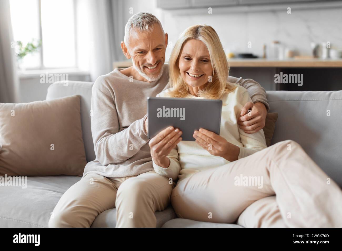 Positive retired couple using digital tablet at home Stock Photo