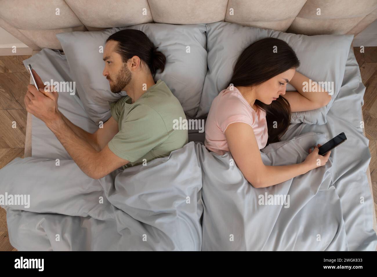 Couple in bed on phones, lying back to back Stock Photo