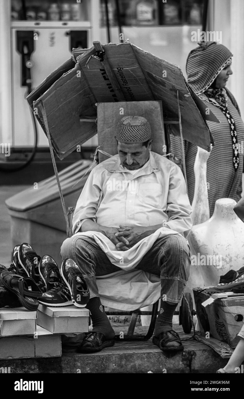 A trader selling shoes takes a nap during a slow day. Rabat, Morocco's capital, rests along the shores of the Bouregreg River and the Atlantic Ocean. It's known for landmarks that speak to its Islamic and French-colonial heritage, including the Kasbah of the Udayas. This Berber-era royal fort is surrounded by formal French-designed gardens and overlooks the ocean. The city's iconic Hassan Tower, a 12th-century minaret, soars above the ruins of a mosque. Morocco. Stock Photo
