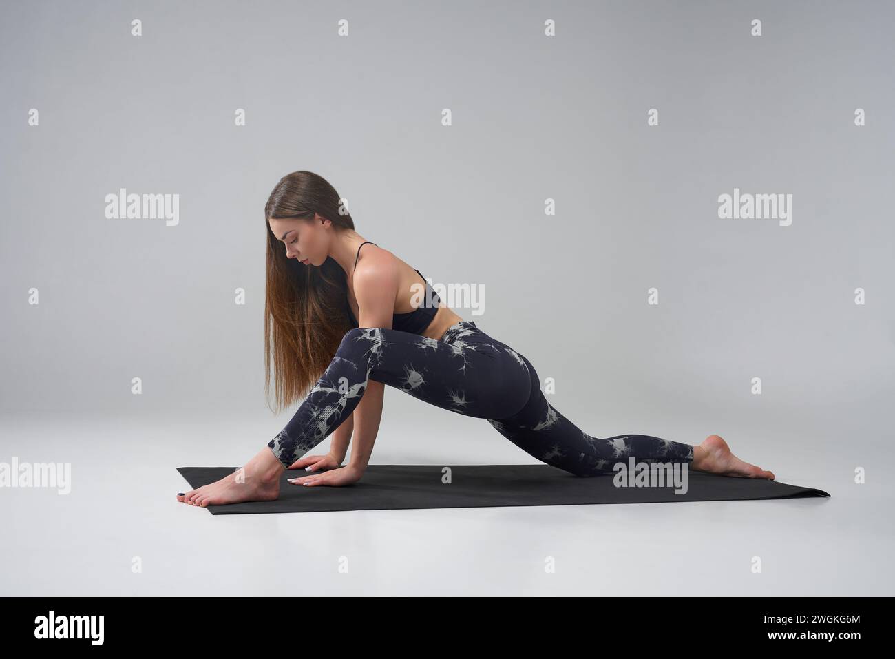 focused caucasian girl doing lizard position of yoga in studio side view of pretty female wearing leggings looking at camera while practicing yoga on mat isolated on grey background yoga concept 2WGKG6M