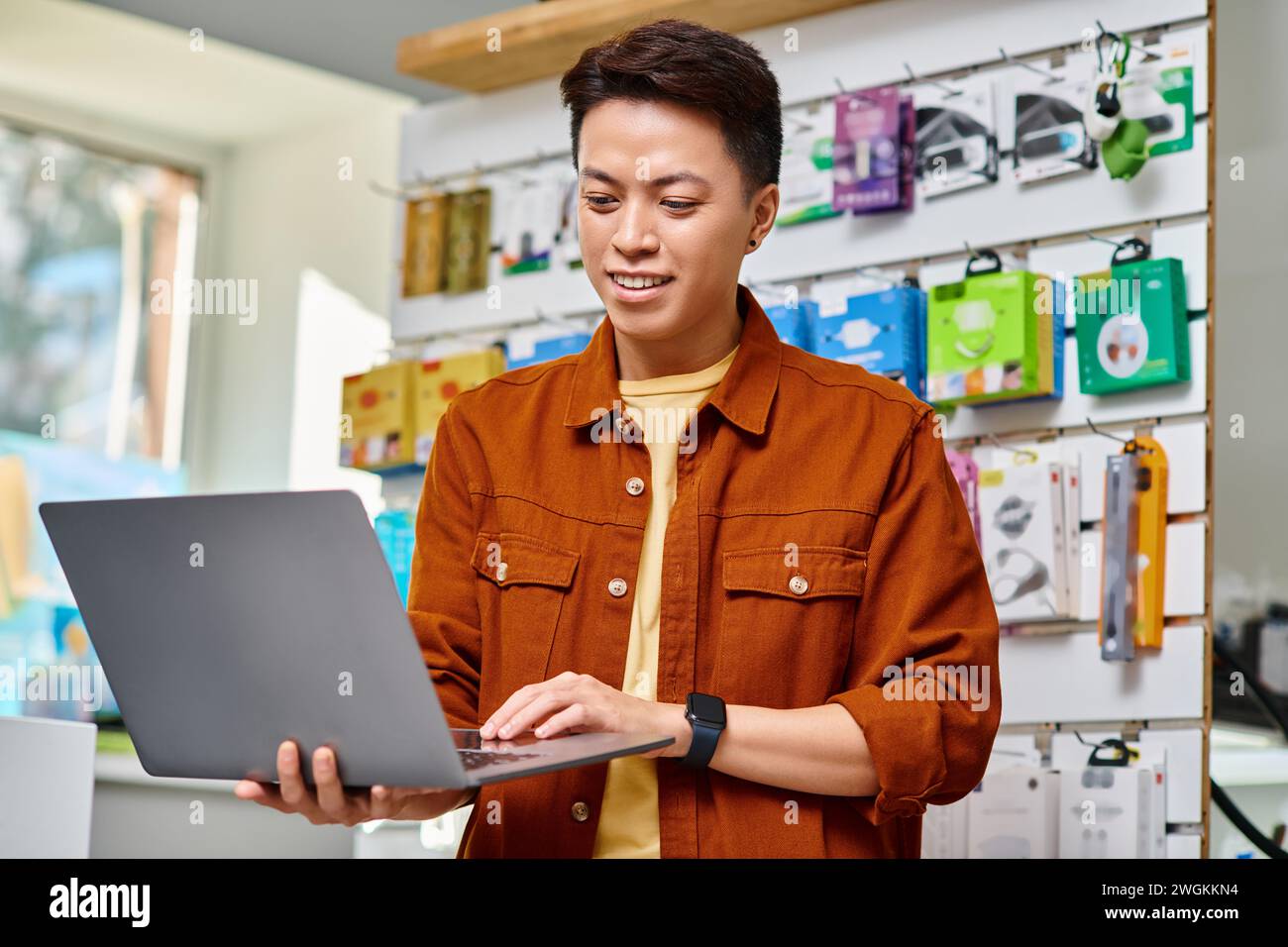 happy asian entrepreneur using laptop standing in own electronics store, small business concept Stock Photo