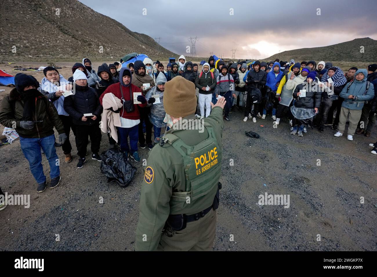 A Border Patrol agent asks asylum-seeking migrants to line up in a ...