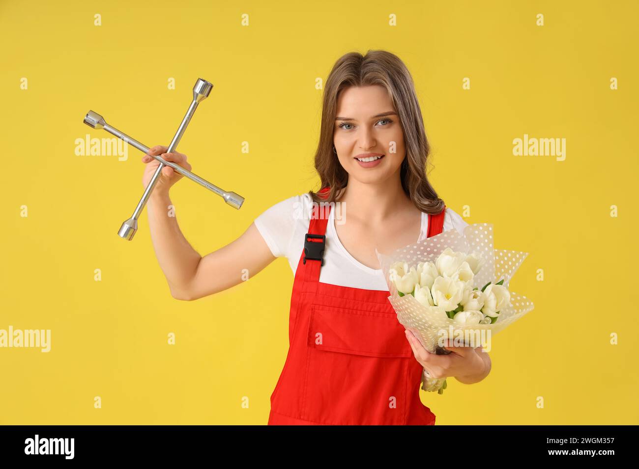 Female mechanic with cross wrench and bouquet of white tulips on yellow ...