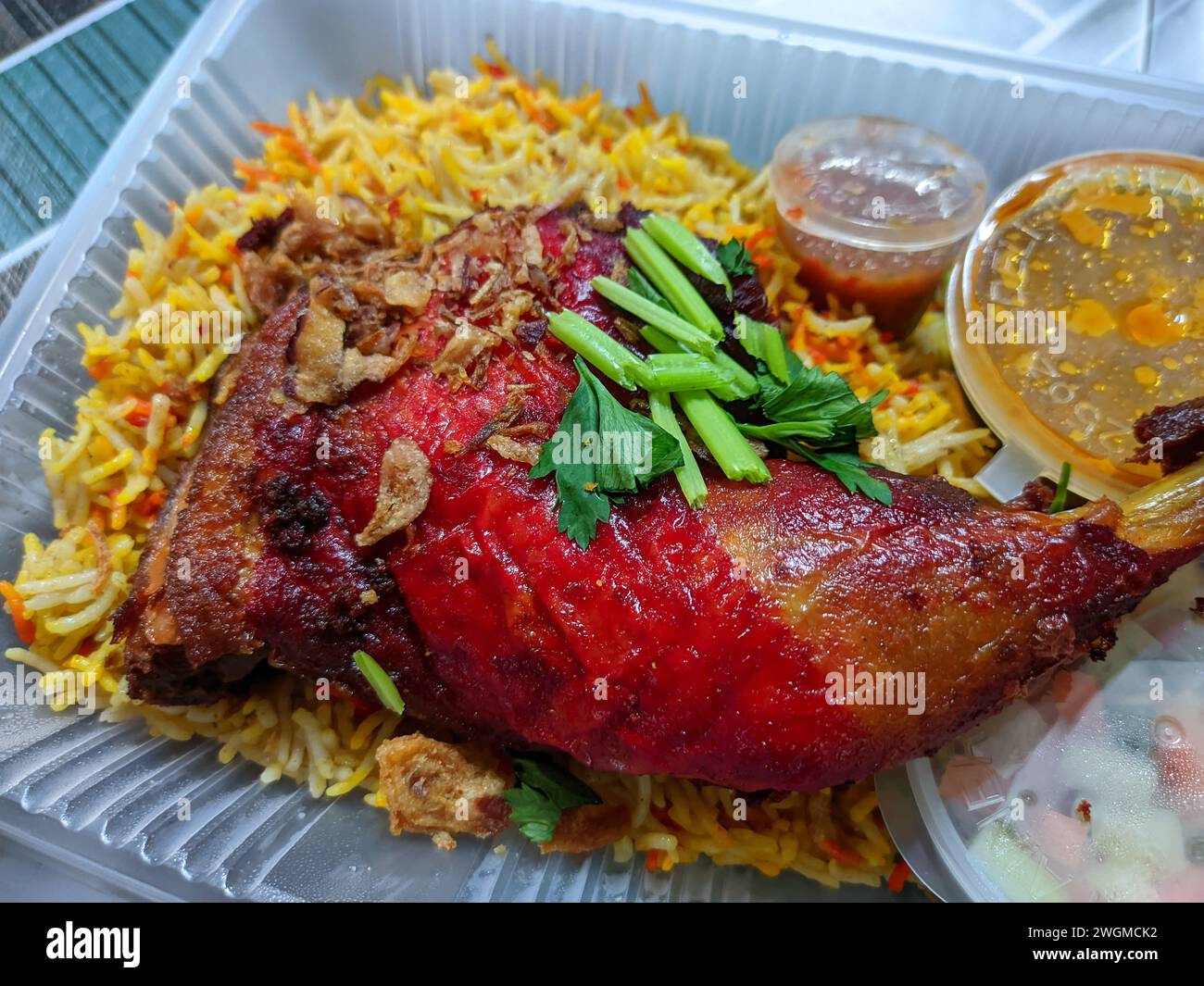 Top view arabic rice with red chicken thighs,colorful rice and curry soup in a white plastic container. Stock Photo