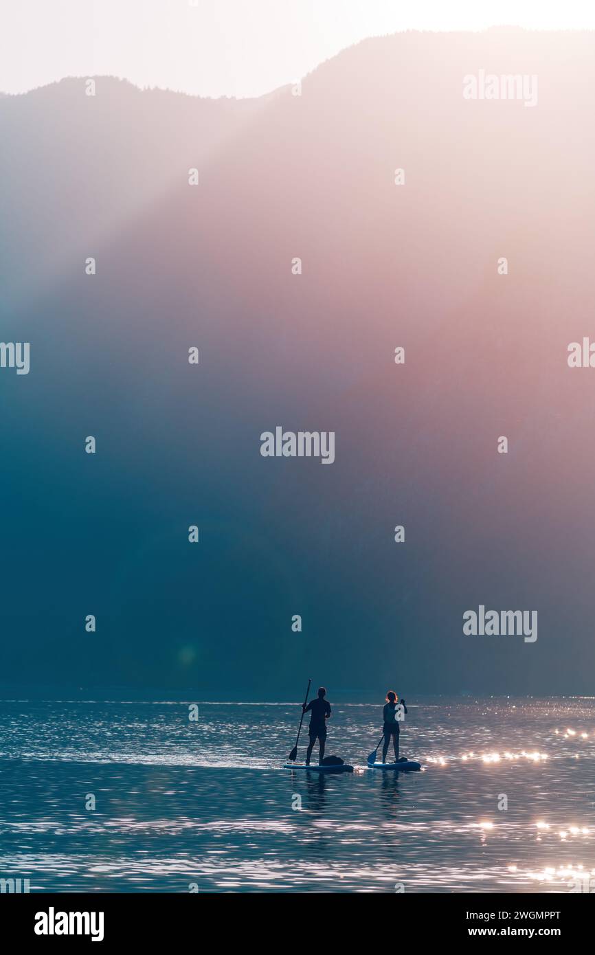 Couple paddle boarding at Lake Bohinj in summer, back lit image with lens flare, selective focus Stock Photo