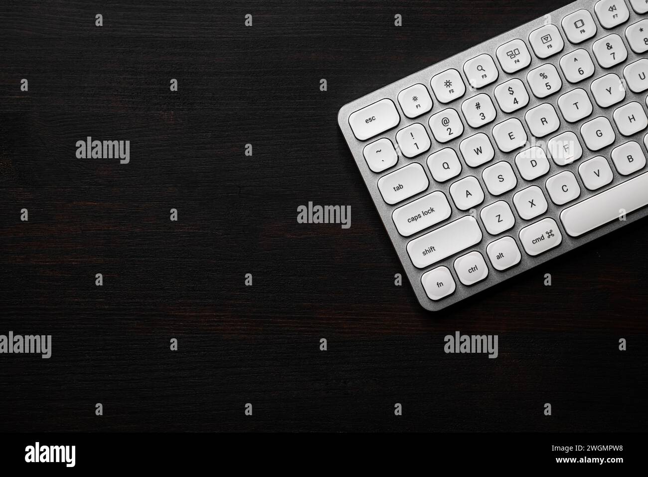 Modern white aluminum computer keyboard on dark wooden home office desk as copy space, top view Stock Photo