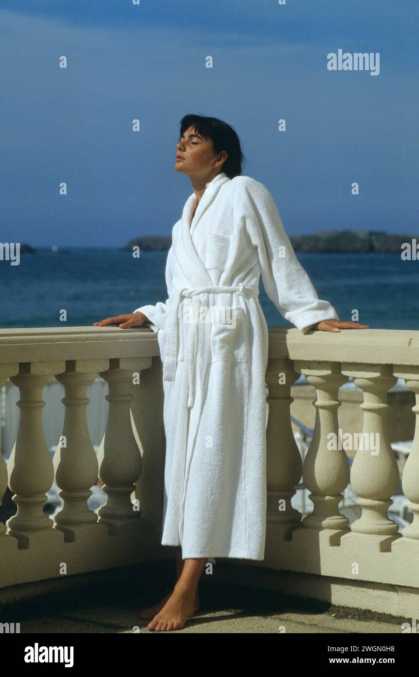 pretty dark hair young woman standup on terrasse balcony beauty silhouette with white bath suit taking sunny day to breathe marine blue sky background Stock Photo