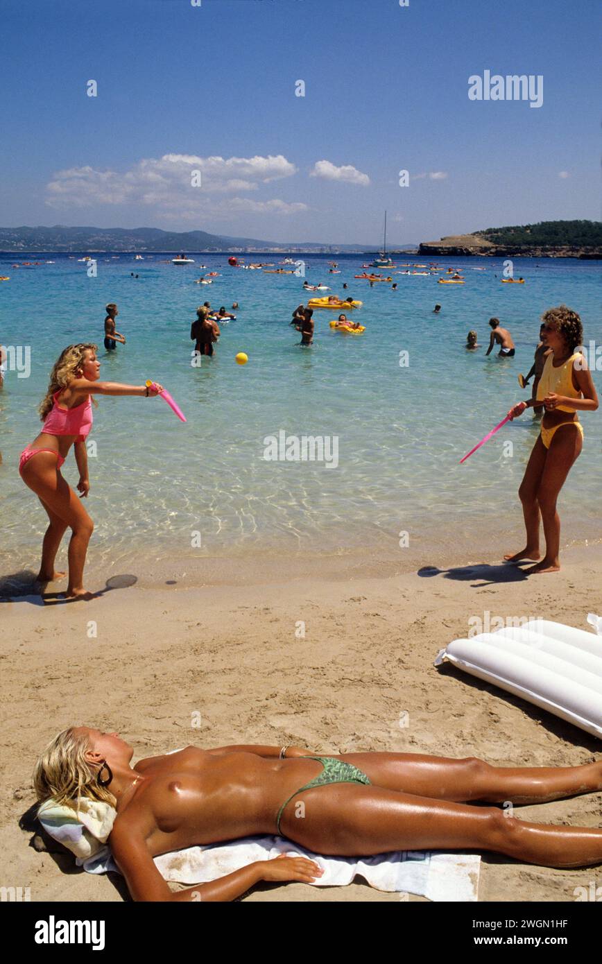 2 blond hair attractive woman playing beach ball profile front camera white sand beach, blue sky summer holidays healthy body Stock Photo