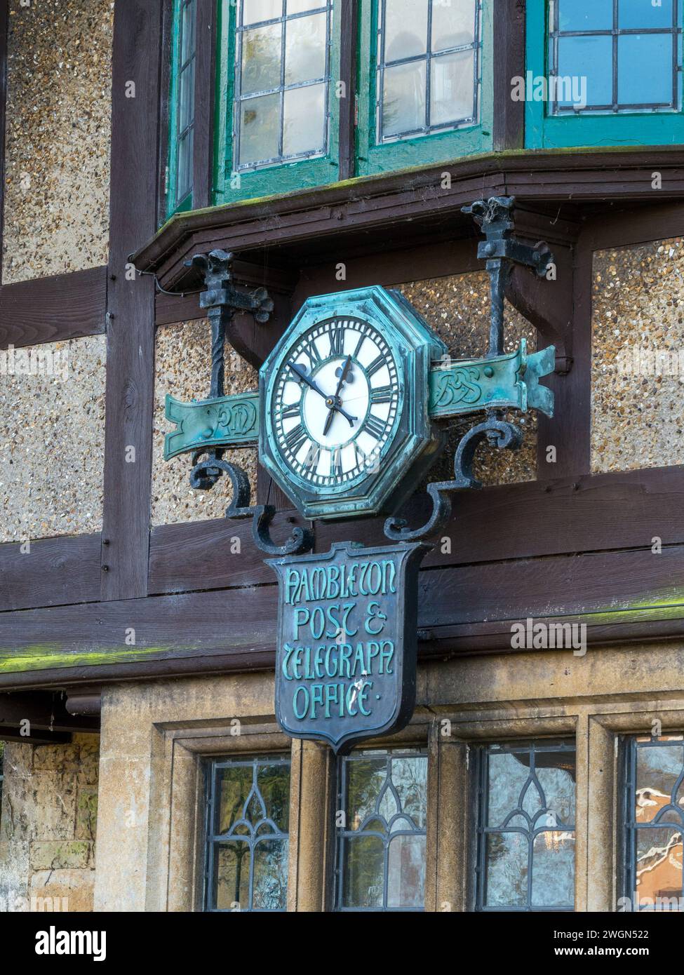 Old village clock with Roman numerals set in wrought iron Post and Telegraph office sign, Hambleton, Rutland, England, UK. Stock Photo