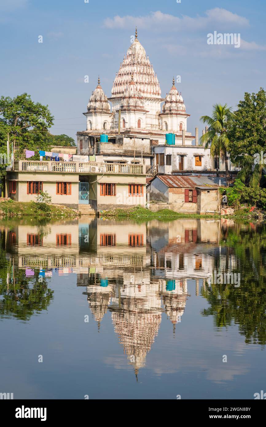 Scenic vertical view of ancient Bhubaneshwar Shiva temple and houses with reflection in lake, Puthia, Rajshahi, Bangladesh Stock Photo