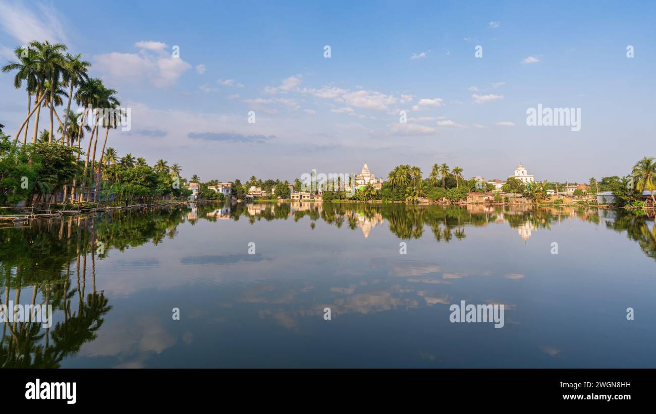 Scenic landscape panorama with Bhubaneshwar Shiva temple and houses reflection in lake, Puthia, Rajshahi, Bangladesh Stock Photo