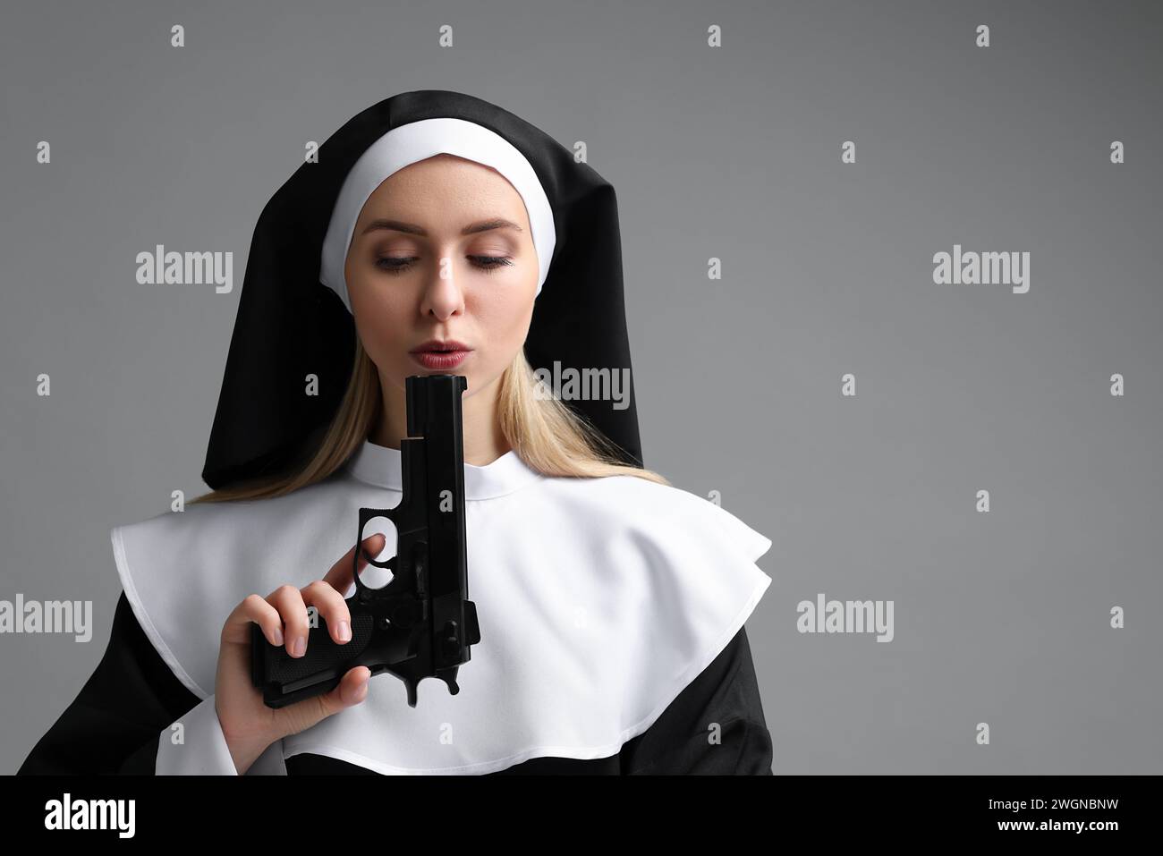 Woman in nun habit holding handgun on grey background. Space for text Stock Photo
