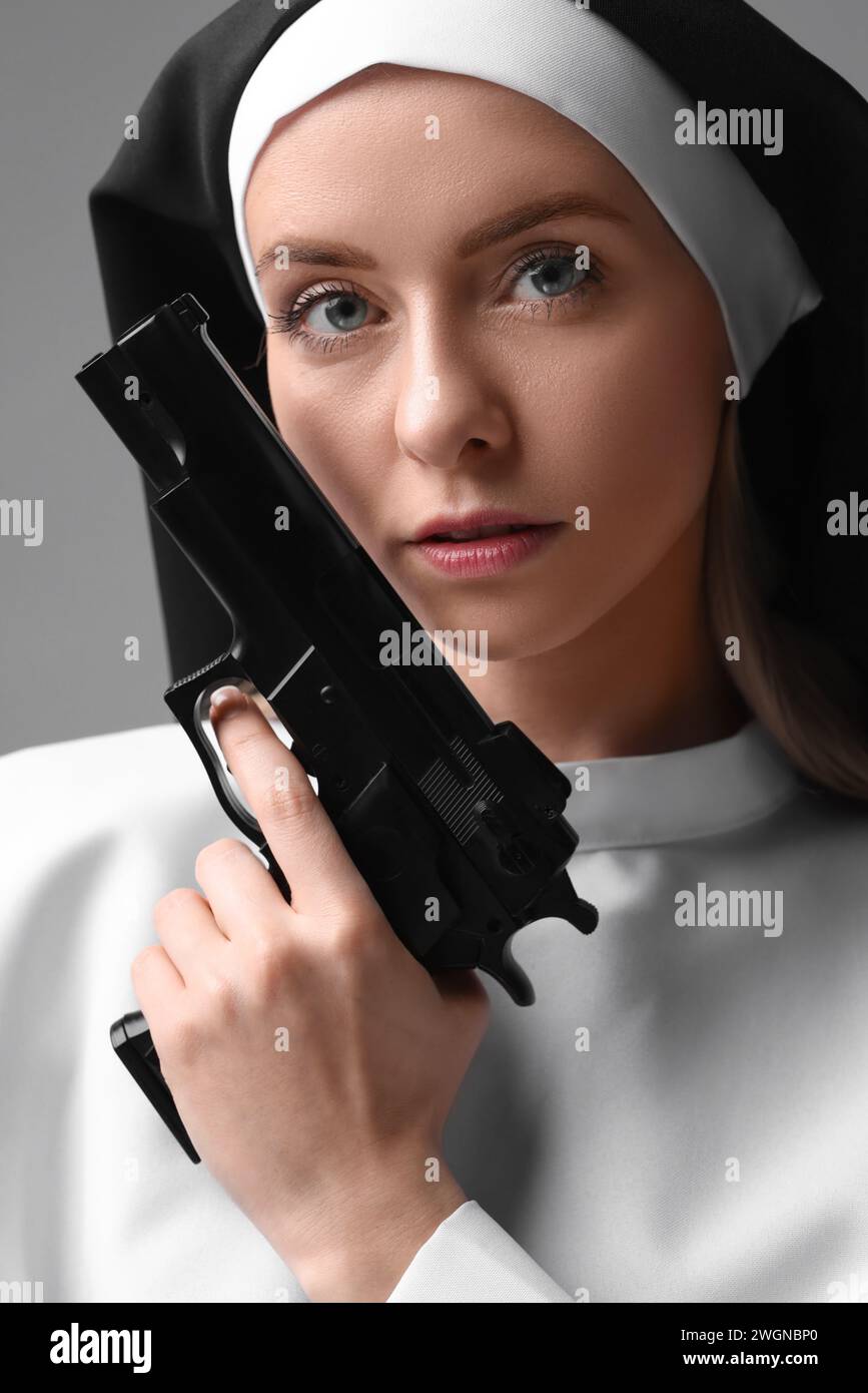 Woman in nun habit holding handgun on grey background, closeup Stock Photo