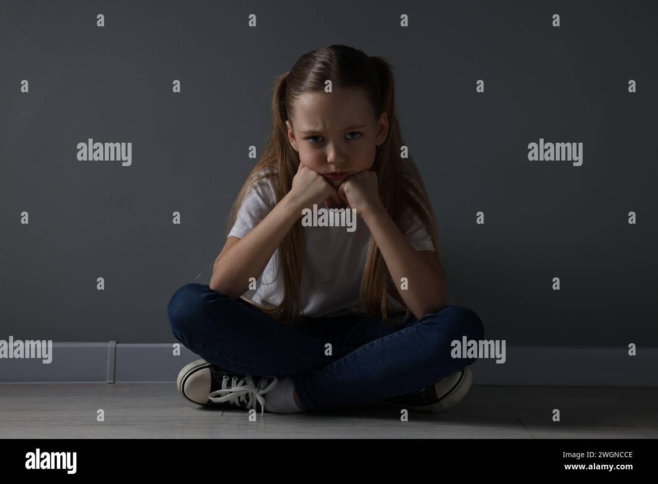 Sad girl sitting on floor near dark grey wall indoors Stock Photo - Alamy