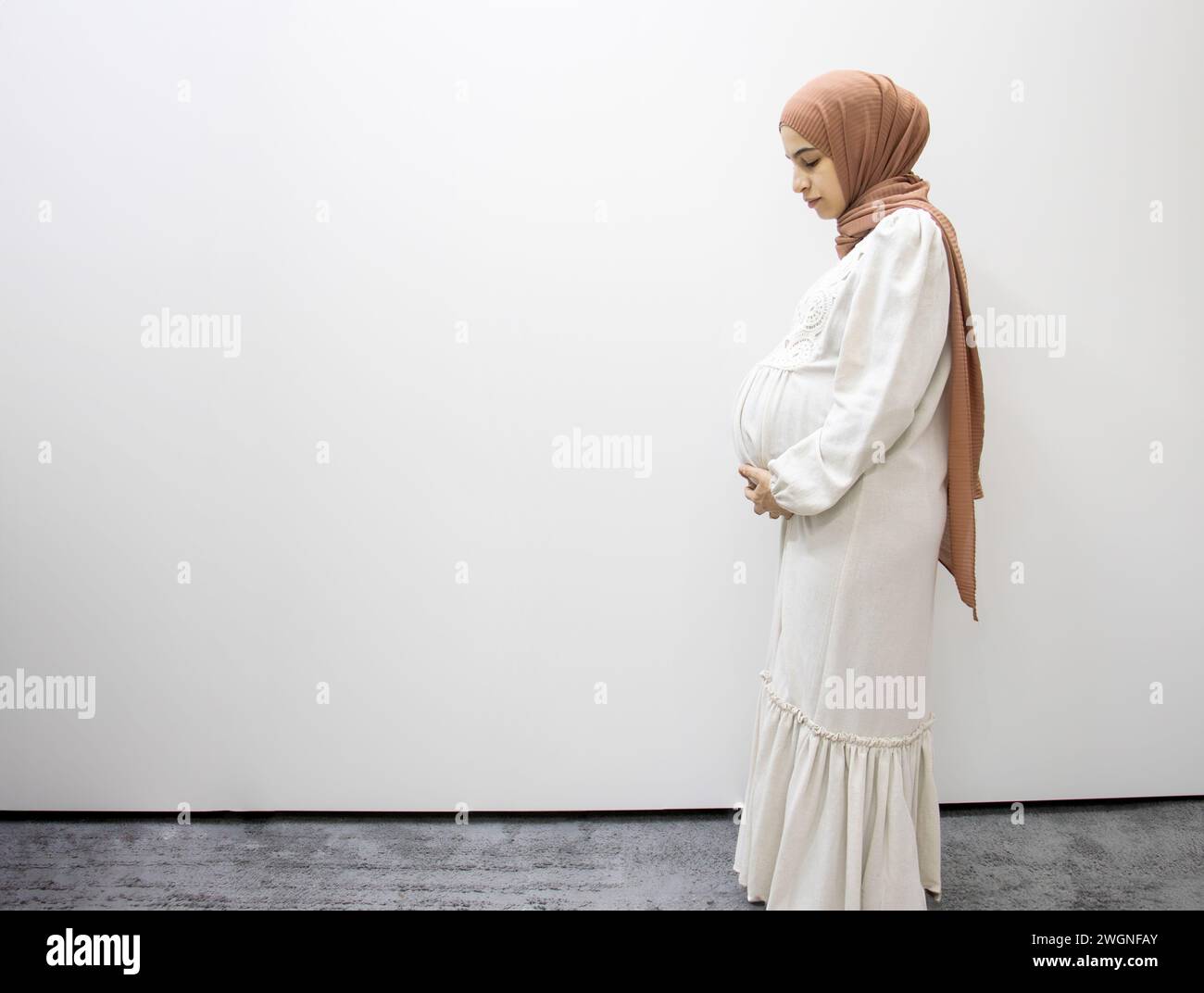 Pregnant Arabic Muslim Female On Isolated White Background Touching Her Tummy Showing Her Body