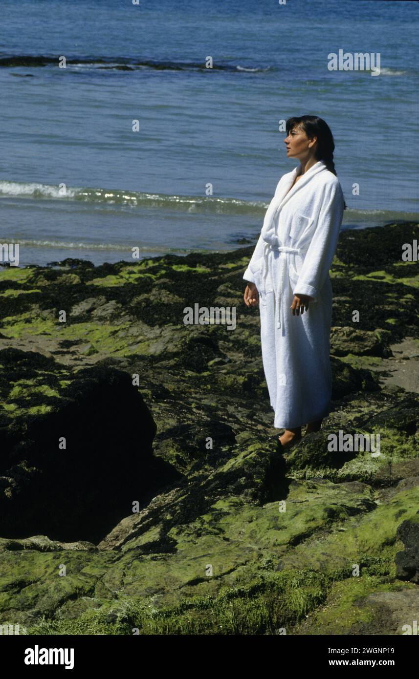 pretty dark hair young woman walking on seagreenon rocks france St Malo with white bath coat Stock Photo