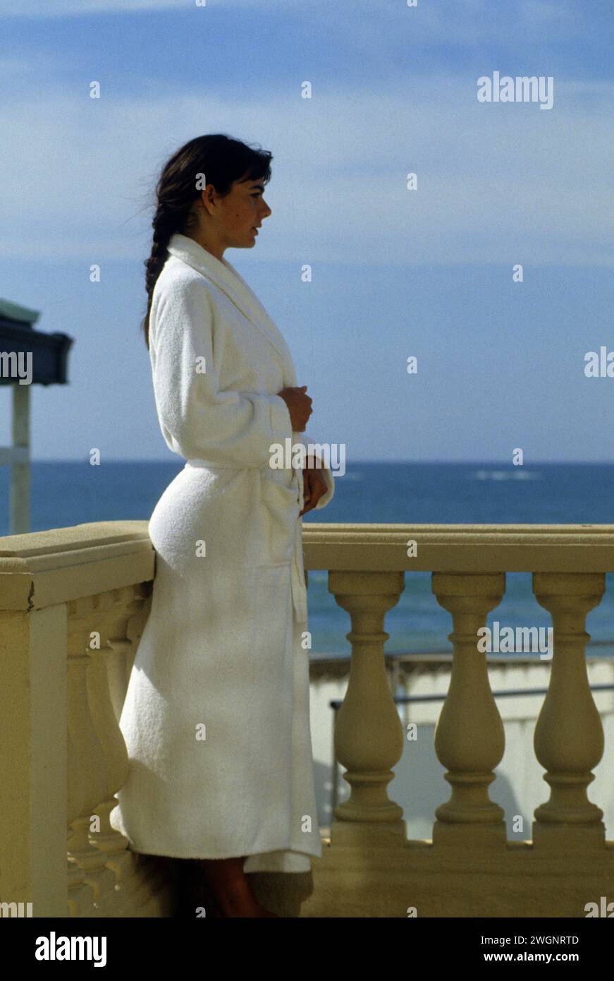 pretty dark hair young woman standup on terrasse balcony beauty silhouette with white bath suit taking sunny day to breathe marine blue sky background Stock Photo