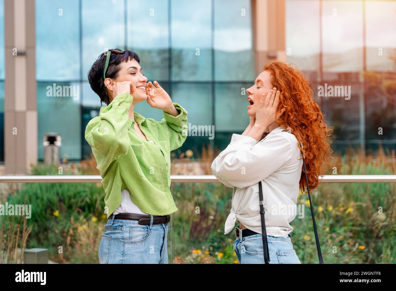 two girls covered their ears with their hands, screaming and do not want to listen to each other Stock Photo