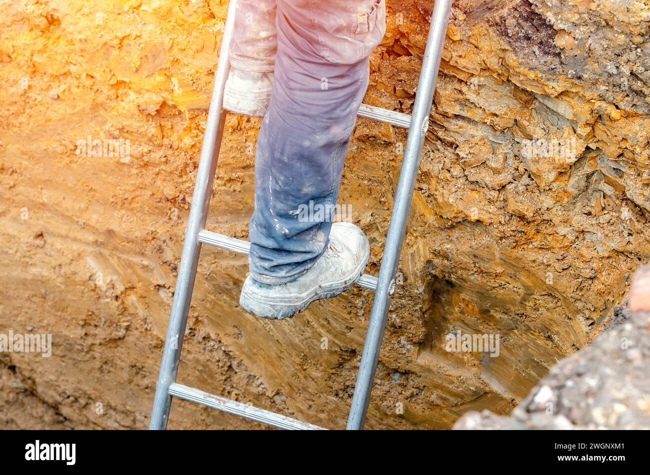 Builder going up the ladder to get out of trench Stock Photo