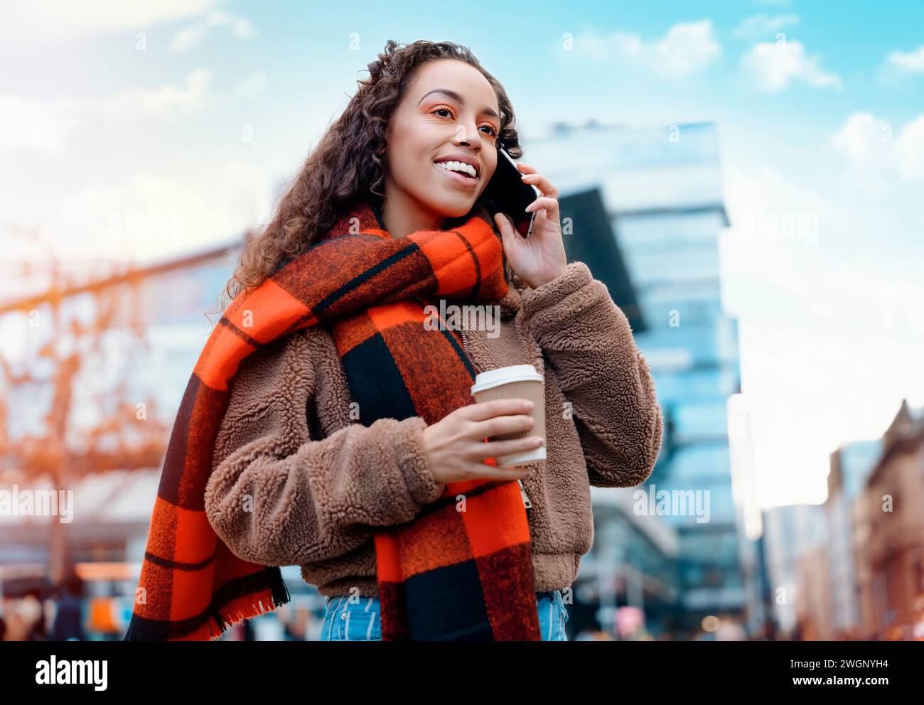 Outdoor portrait of a happy  woman using a mobile phone and drinking coffee in a Europe city Stock Photo