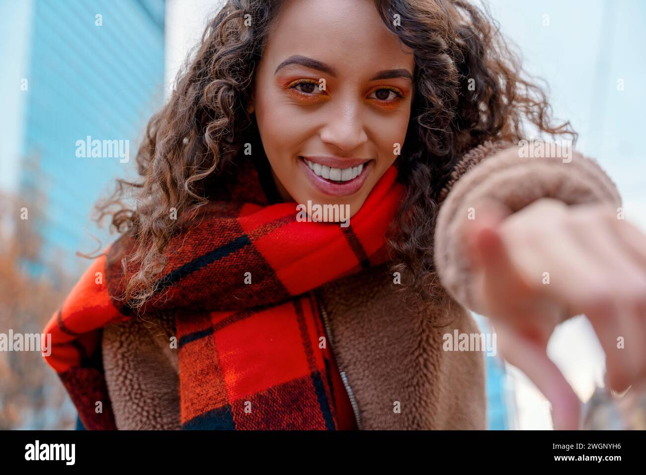 young mixed race smiling woman in coat and orange scarf  pointing her finger at the camera as in a screen Stock Photo