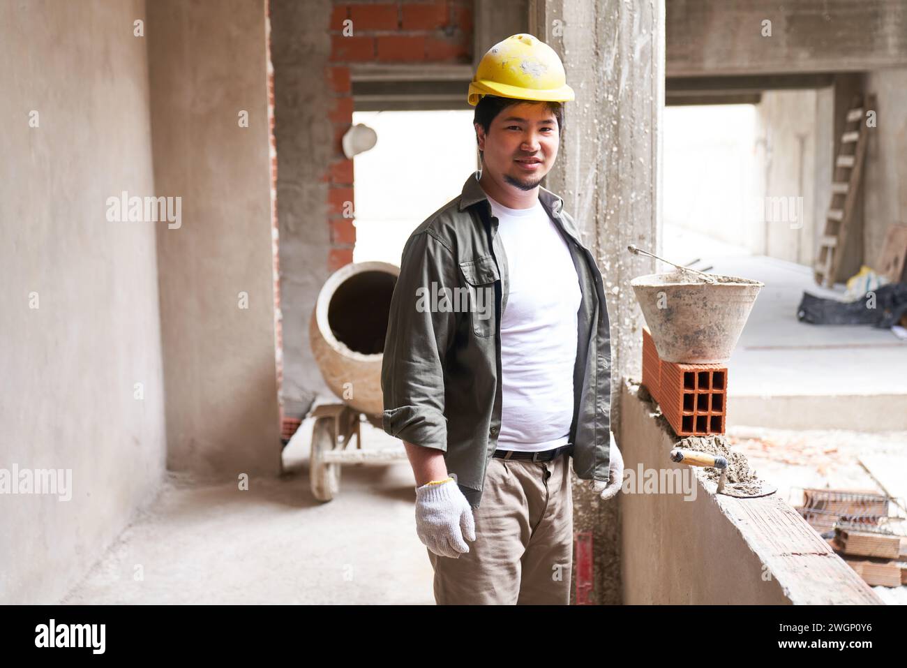 Smiling young bricklayer by incomplete wall Stock Photo