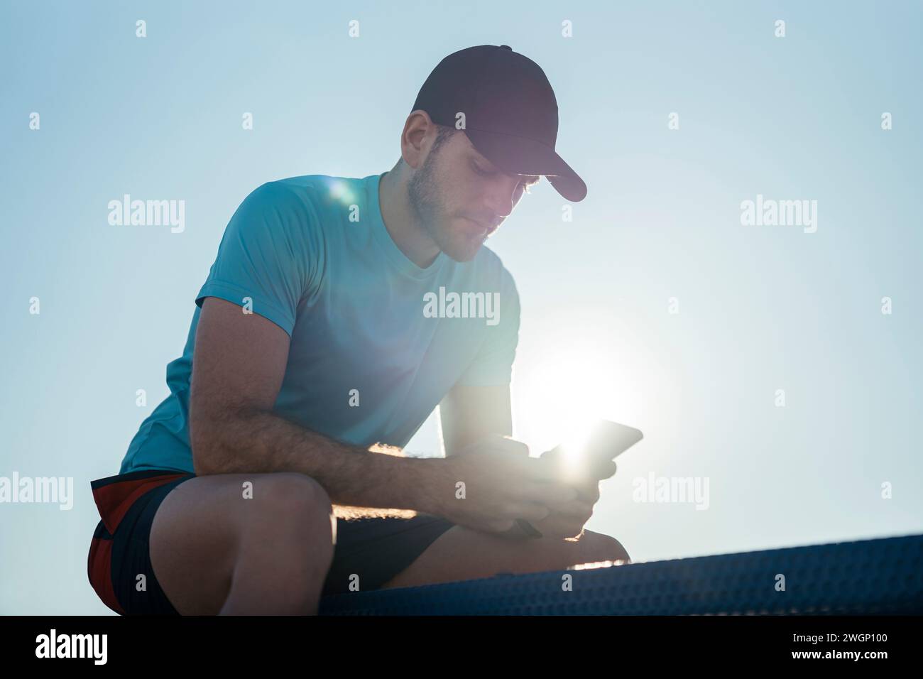 A man in a hat using cell phone, sitting on a bench Stock Photo