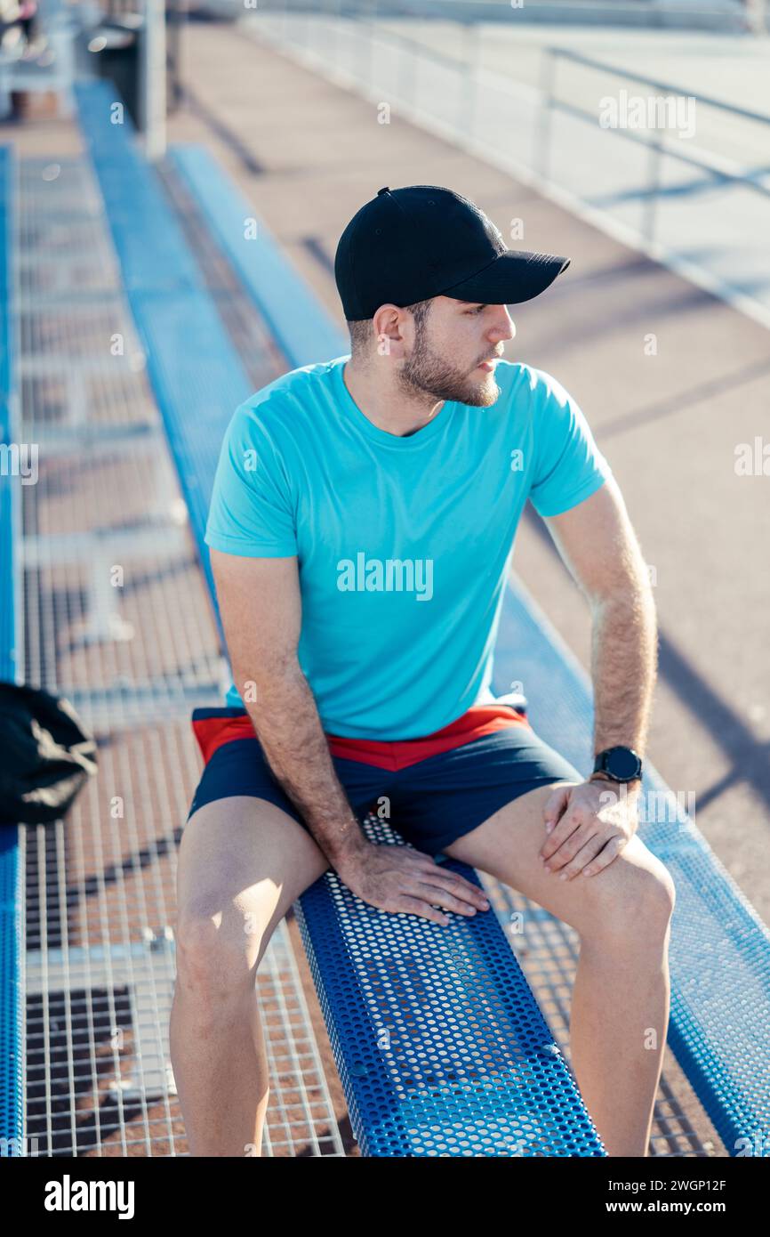 A man sitting on a blue bench, wearing a cap Stock Photo