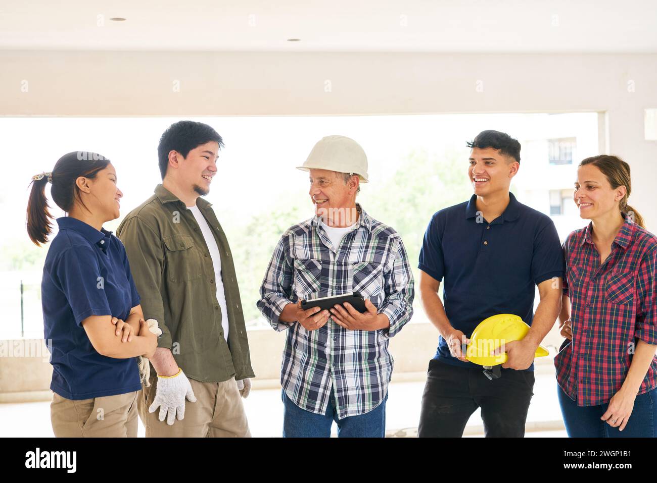 Smiling contractor holding tablet PC discussing with team Stock Photo