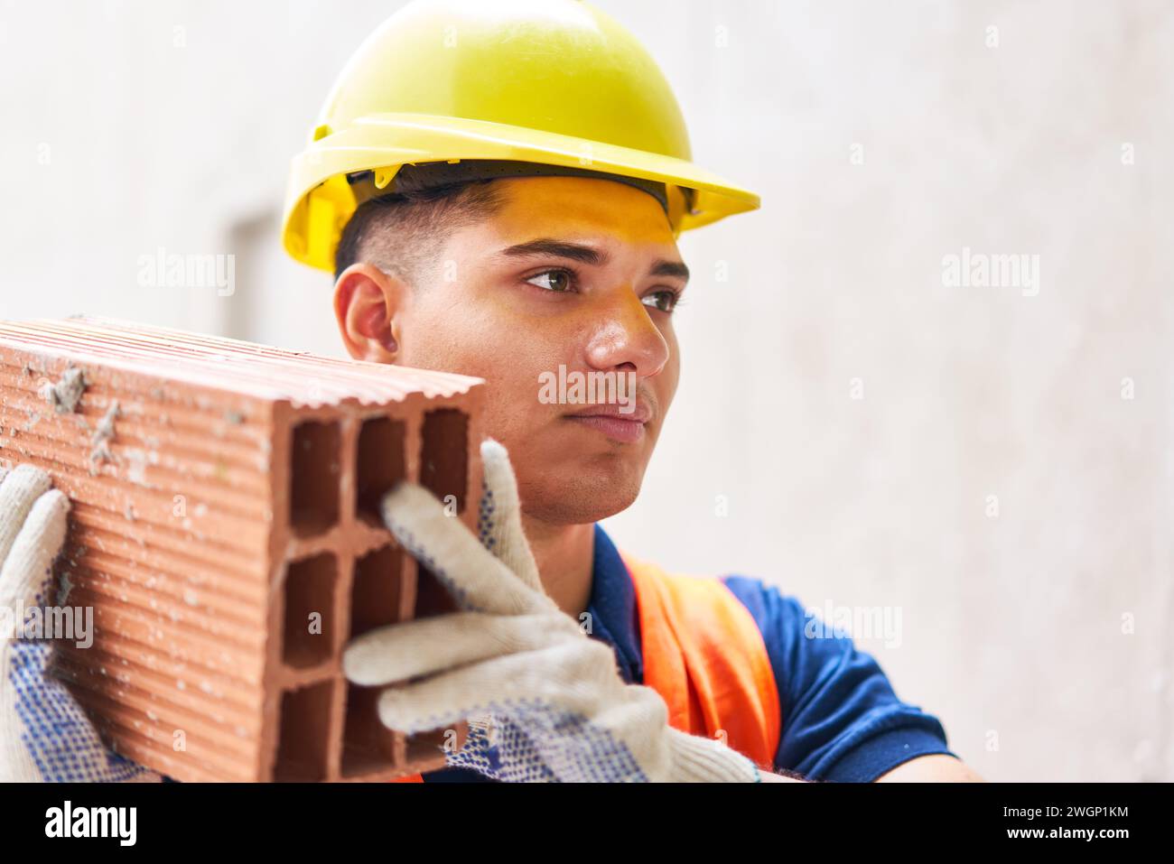 Confident male bricklayer wearing hardhat carrying brick Stock Photo