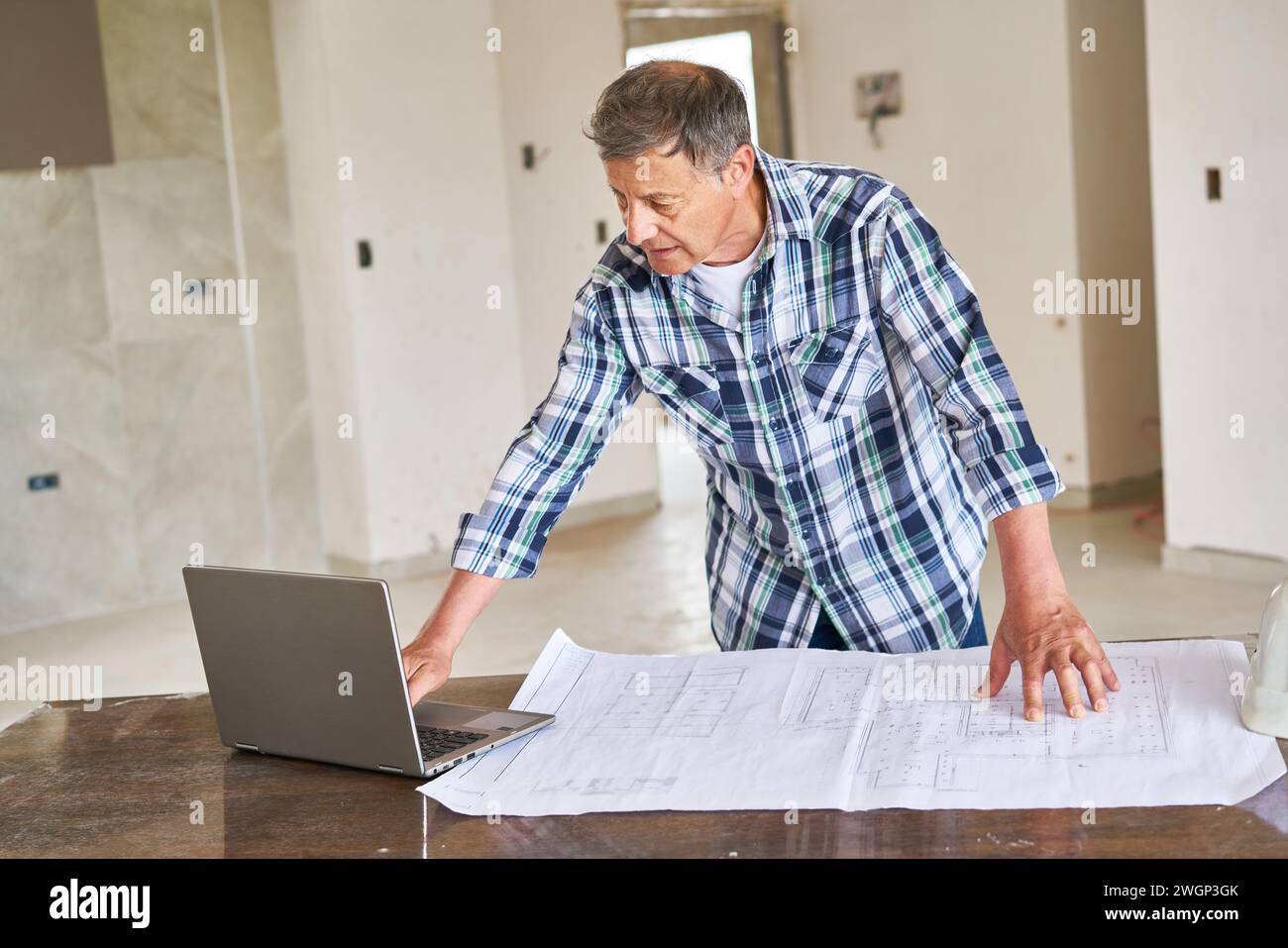 Senior architect using laptop by blueprint at desk Stock Photo