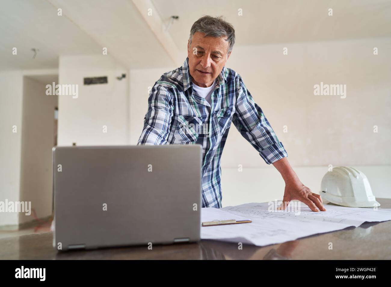 Senior architect using laptop by blueprint at desk Stock Photo