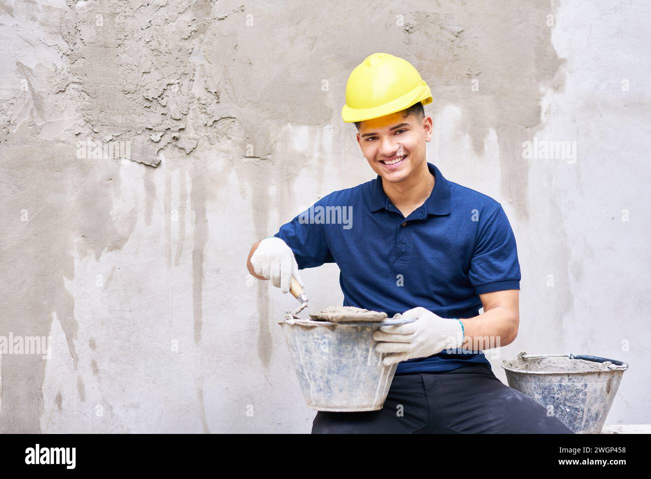 Smiling male worker sitting with bucket and mortar Stock Photo