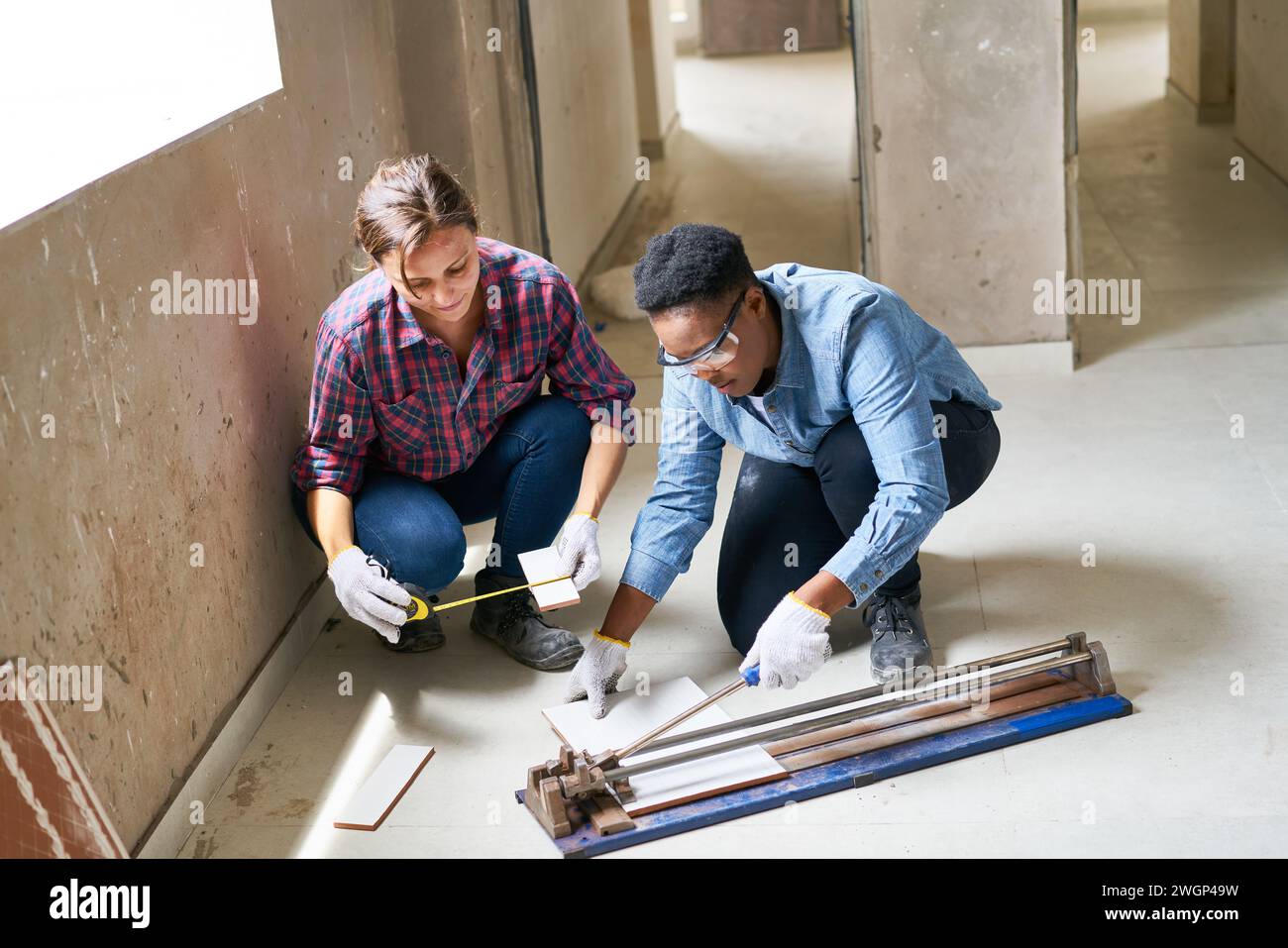 Female coworkers measuring and cutting plank Stock Photo