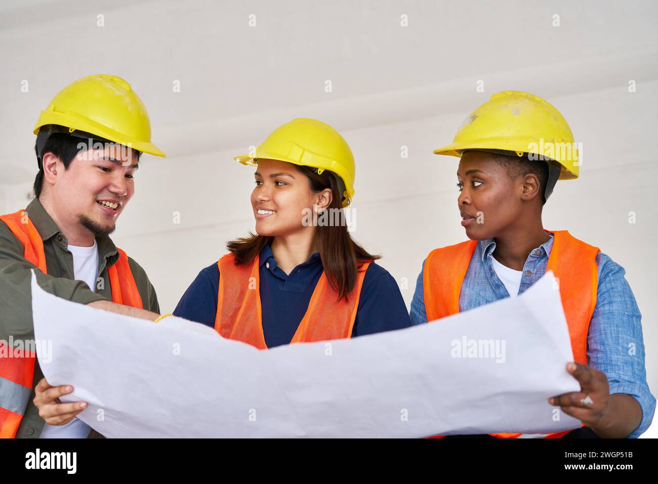 Smiling diverse team discussing while examining blueprint Stock Photo